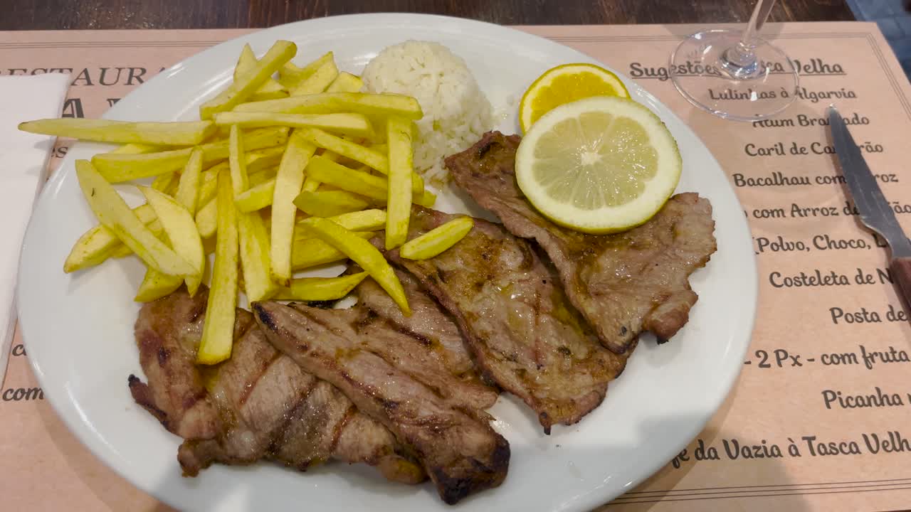 A delicious plate of grilled meat served with crispy fries, rice, and fresh lemon slices. The savory dish offers a hearty meal perfect for a satisfying lunch or dinner.