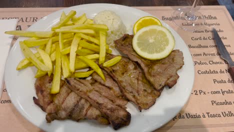 a delicious plate of grilled meat served with crispy fries, rice, and fresh lemon slices. the savory dish offers a hearty meal perfect for a satisfying lunch or dinner.