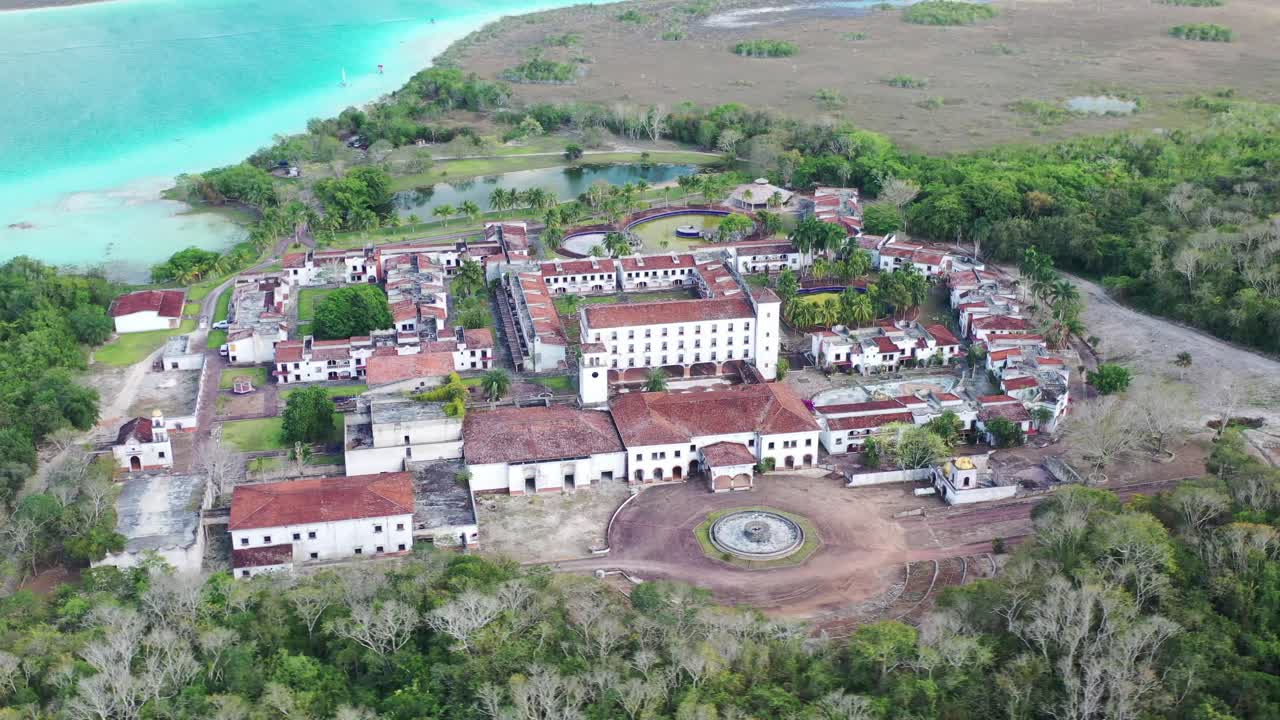 Ripresa aerea con drone dell'hotel fantasma abbandonato accanto alla Laguna dei Sette Colori a Bacalar, Messico. Rovine uniche circondate da acqua turchese, natura tropicale e scenari di viaggio iconici