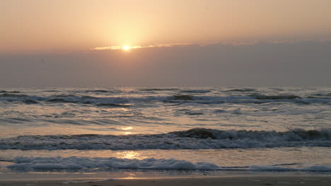 gentle waves roll on a serene beach at sunrise with golden light reflecting on the water