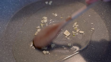 mixing garlic and oil on a cooking pan with a wooden spoon