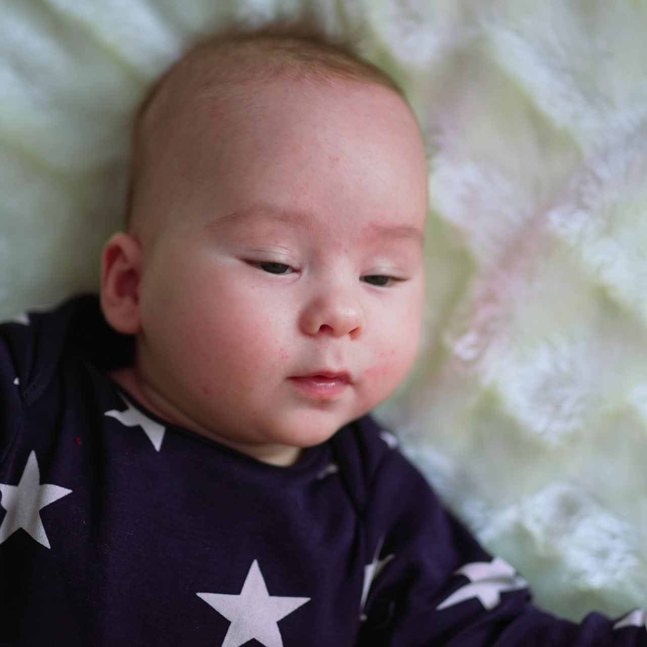 Caucasian infant boy lies on bed moving actively with his hands. Portrait of a beautiful child lying on bed. Close up