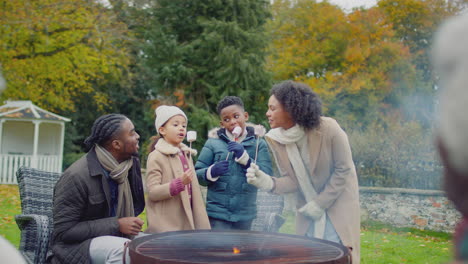 Mehrgenerationenfamilie-Beim-Toasten-Und-Essen-Von-Marshmallows,-Stehend-Um-Feuerstelle-Oder-Grill-Im-Heimischen-Garten-–-Aufnahme-In-Zeitlupe