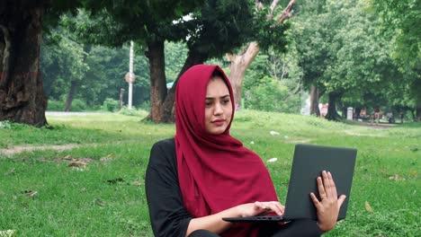 Happy-Afghan-woman-in-hijab-working-on-laptop-computer-on-green-lawn-near-busy-road