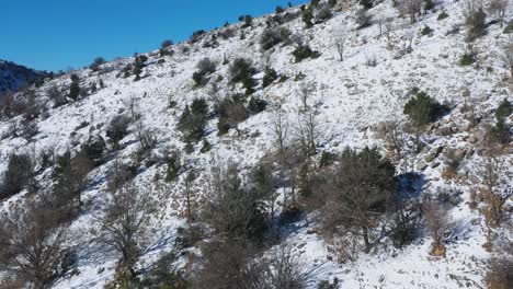 Drone-flight-over-a-snow-covered-rugged-alpine-mountain-with-blue-sky-at-Mt,-Hermon-in-the-Golan-Heights,-Israel