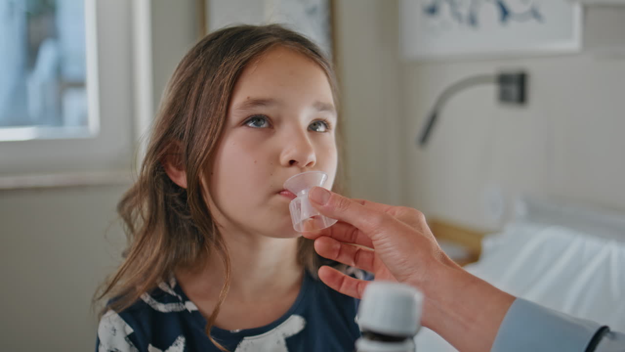 Sick child taking medicine at white bedroom closeup. Mom giving mixture to kid