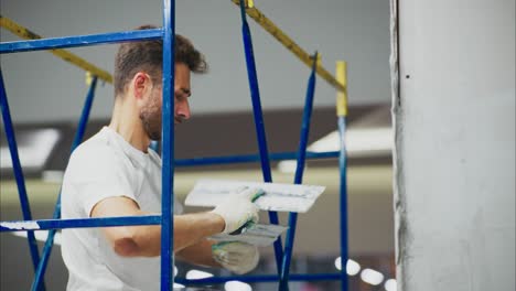 A dedicated worker skillfully applies plaster to a wall while using a scaffold, showcasing the art of renovation and the transformation of indoor spaces