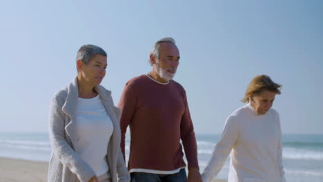 Peaceful-senior-friends-walking-along-ocean-shore-and-talking