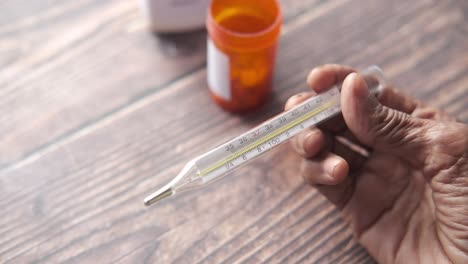 hand holding a thermometer with pills in the background