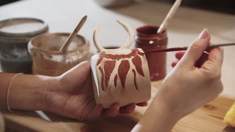 young woman potter painting on the ceramic cup with a brush