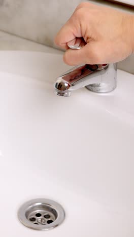 hand opening and closing water faucet in bathroom sink