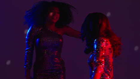 close up of two women in nightclub bar or disco dancing with falling confetti and sparkling lights