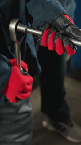 primer plano de un mecánico con guantes rojos apretando pernos en el bloque del motor, con las piernas de otra persona visibles, trabajando juntos en un taller ocupado