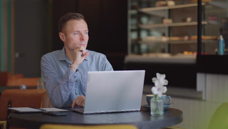 Nachdenklicher,-Ernster-Junger-Mann,-Studentischer-Schriftsteller,-Sitzt-Am-Schreibtisch-Im-Heimbüro-Mit-Laptop-Und-Denkt-An-Inspiration,-Suche,-Problem,-Lösung,-Ideen,-Gedankenverloren,-Konzept,-Träumend-Und-Wegschauend