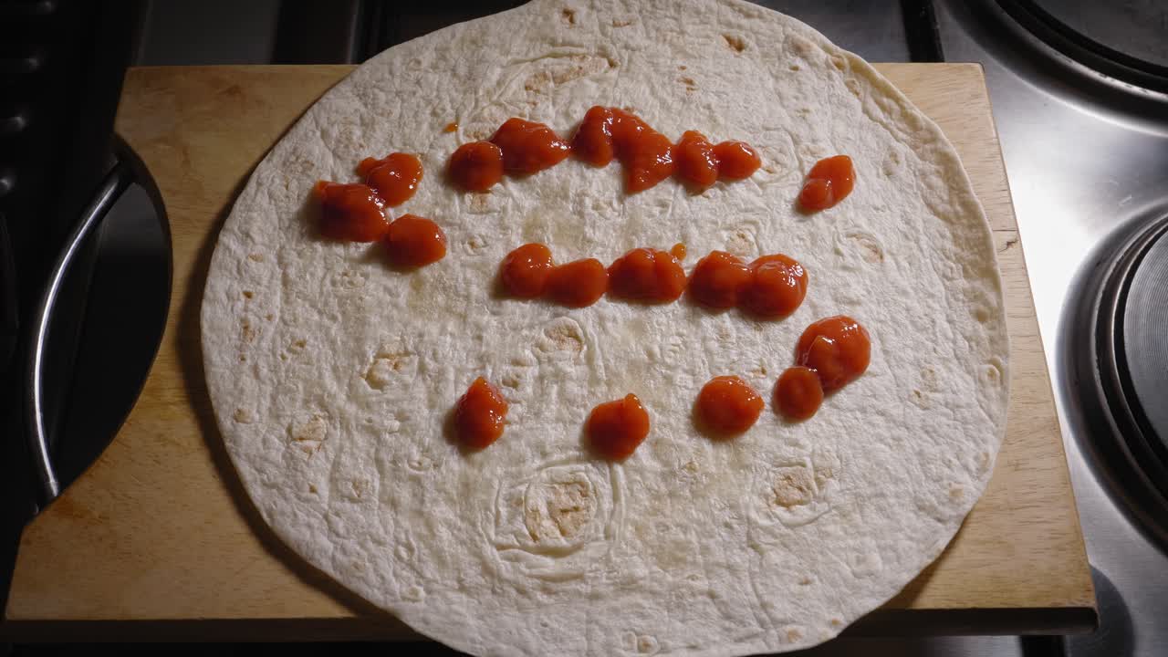 un primer plano de una sabrosa salsa de tomate que se vierte estratégicamente sobre una envoltura redonda de harina de trigo, la fuente proporciona la capa base de sabor para una deliciosa tortilla de hot dog