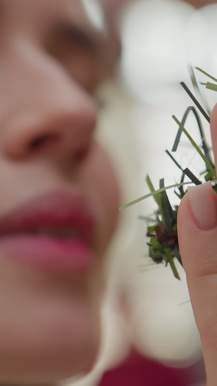Close-up of white lady affectionately holding Christmas tree while smelling it, background features soft bokeh light effect, with unclear figure moving