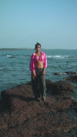 standing man on rocky coastline, gazing at the sea under clear blue sky