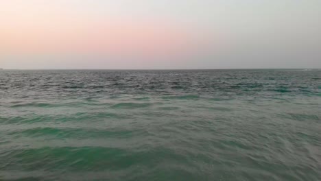 drone flies over calm waves from the persian c during a hazy evening, aerial