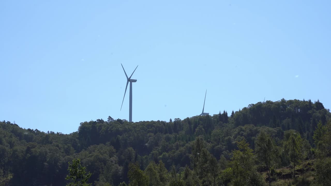 Massive wind turbines rotating on top of hill at island Fitjar in Norway - Static with pollen flying around in lush greenery area during summer
