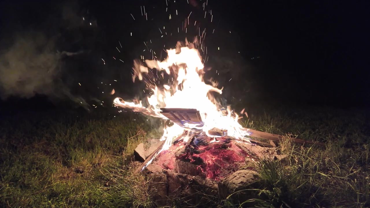 Fogueira vibrante com chamas dançantes e faíscas ascendentes iluminando um prado gramado tranquilo. Uma atmosfera relaxante de natureza selvagem adequada para conteúdo de estilo de vida de camping, mochilão e sobrevivência ao ar livre.