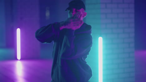 Ein-Mann-Aus-Stahl-Tanzt-Hip-Hop-Freestyle-Im-Modernen-Stil-In-Einer-Halle-Mit-Neonlicht-In-Violett-blauen-Farben.-Männlicher-Professioneller-Hip-Hop-Tänzer