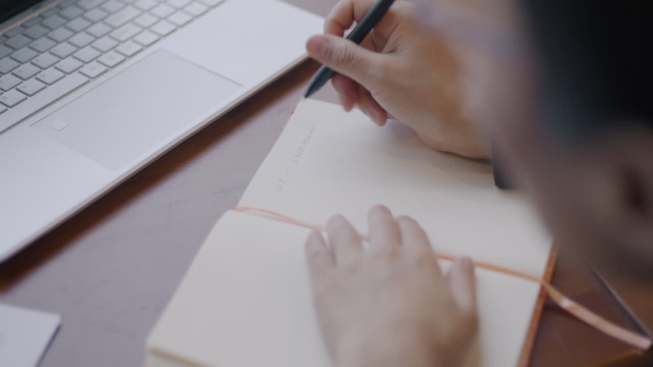 Person Writing in Notebook with Laptop