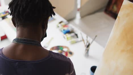 rear view of african american male artist mixing colors in the palette with a brush at art studio