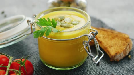 creamy pumpkin soup in jar with bread and tomatoes