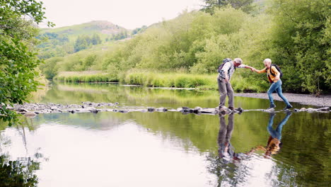 Zeitlupenaufnahme-Eines-älteren-Paares,-Das-Beim-Wandern-Im-Britischen-Seengebiet-Trittsteine-Benutzt,-Um-Den-Fluss-Zu-überqueren