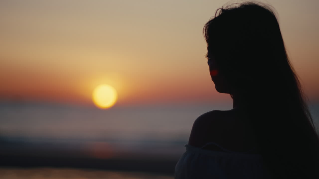 Silhouette di giovane donna che osserva un tramonto luminoso sull'orizzonte dell'oceano dalla spiaggia, momento di pace, calma e tranquillità