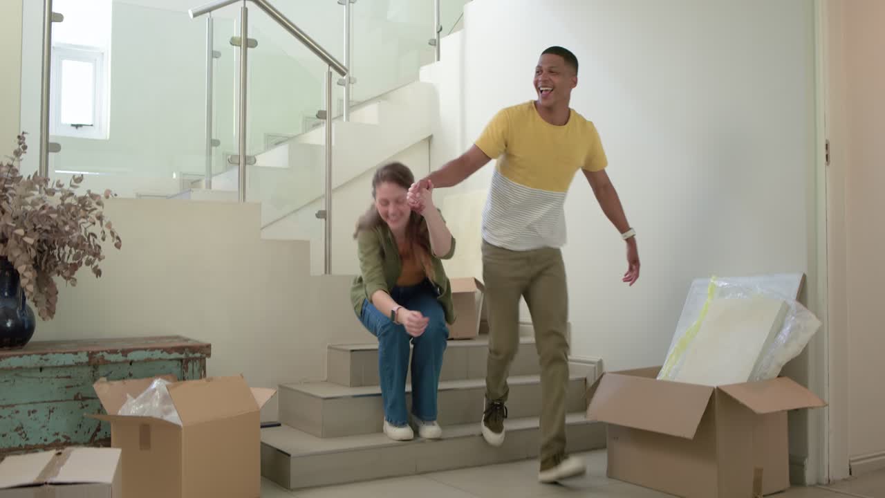 Couple sitting on steps at home laughing at phone, opening box, celebrating move and embracing