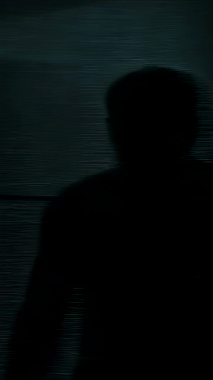 Vertical video: Standing backlit man shifting and turning head in studio, prompted by teal panel