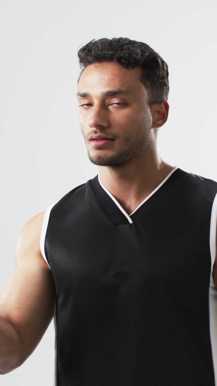 Vertical video: Biracial male athlete posing with volleyball, white background