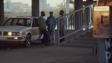 black friends having conversation near car by payphone under bridge