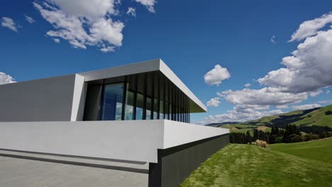 modern house featuring large windows and sleek design, harmoniously blending into a picturesque landscape of rolling hills and a clear blue sky with fluffy clouds