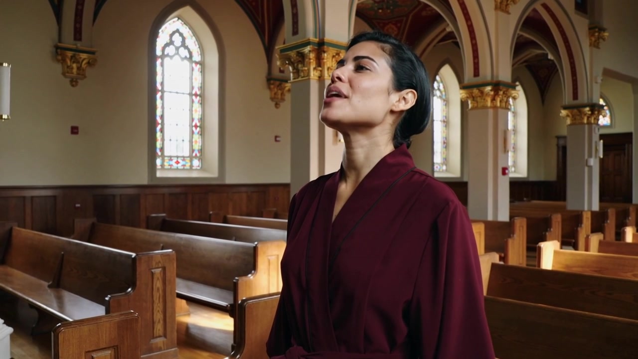 Singing woman in maroon robe looking at stained-glass, projecting solo note in nave, copy space