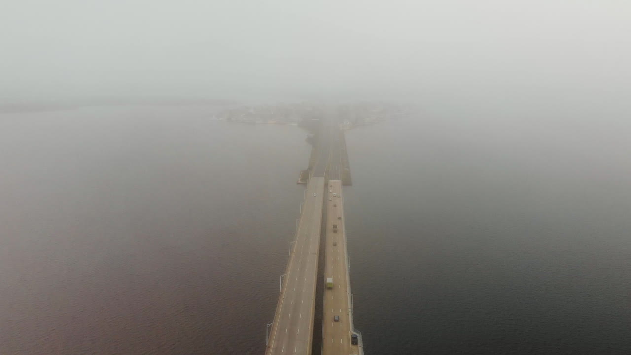 자동차와 트럭의 항공 샷이 거대한 수역 위의 다차선 긴 교량을 가로질러 이동합니다.