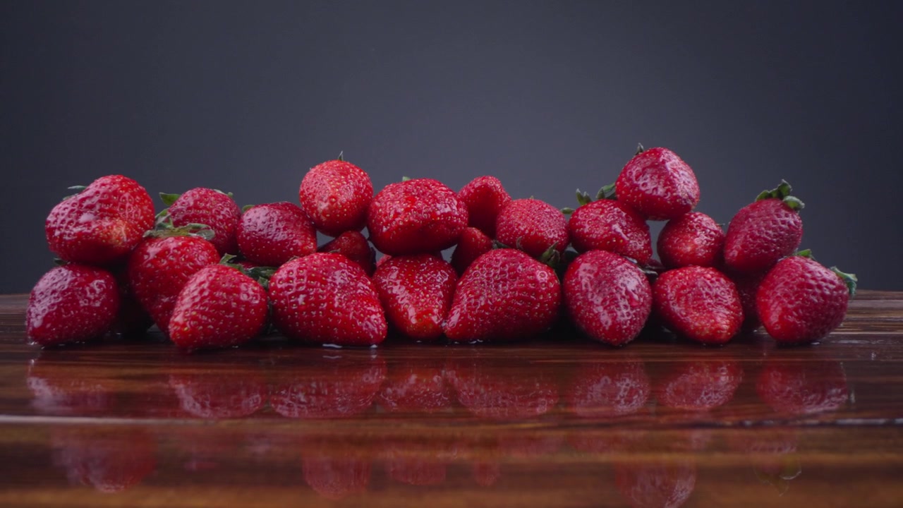 Fresh Red Strawberries with Water Drops on a Reflective Wooden Surface