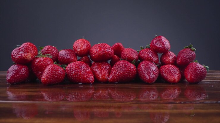Fresh Red Strawberries with Water Drops on a Reflective Wooden Surface