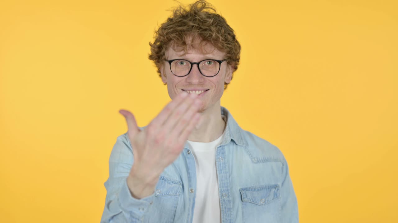 빨간 머리 젊은이가 손을 가리키고 초대하고, 노란색 배경