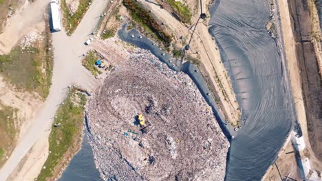 Toma-Amplia-De-Un-Dron-Sobre-Una-Montaña-De-Basura,-Un-Camión-Empuja-La-Basura,-Hay-Muchos-Pájaros-Volando-Sobre-Los-Camiones