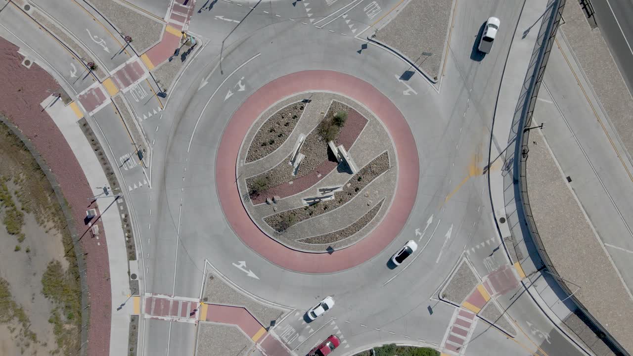 Drone's top-down view of a busy roundabout with personal and commercial vehicles in the early afternoon