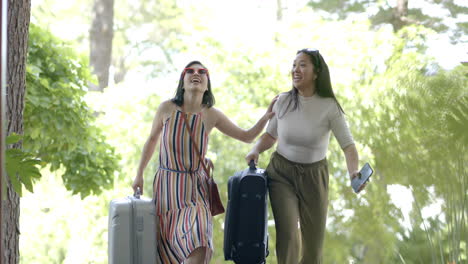 happy asian female friends with suitcases and smartphone walking on stairs of home, slow motion