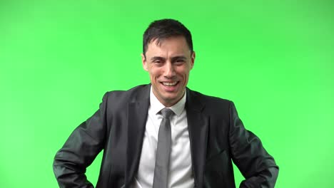 a man in a suit smiling and laughing against a green screen