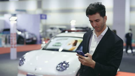 businessman looking at a smartphone at a car show
