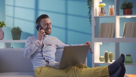 happy elegant businessman working remotely on laptop online at home and talking on friendly phone.