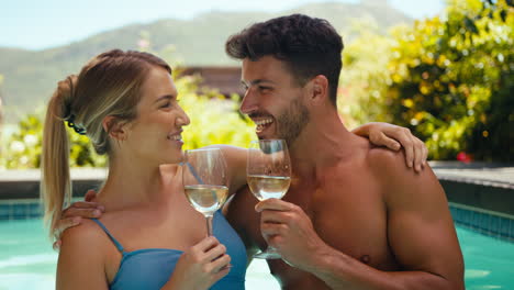 portrait of smiling couple on holiday in swimming pool drinking wine together