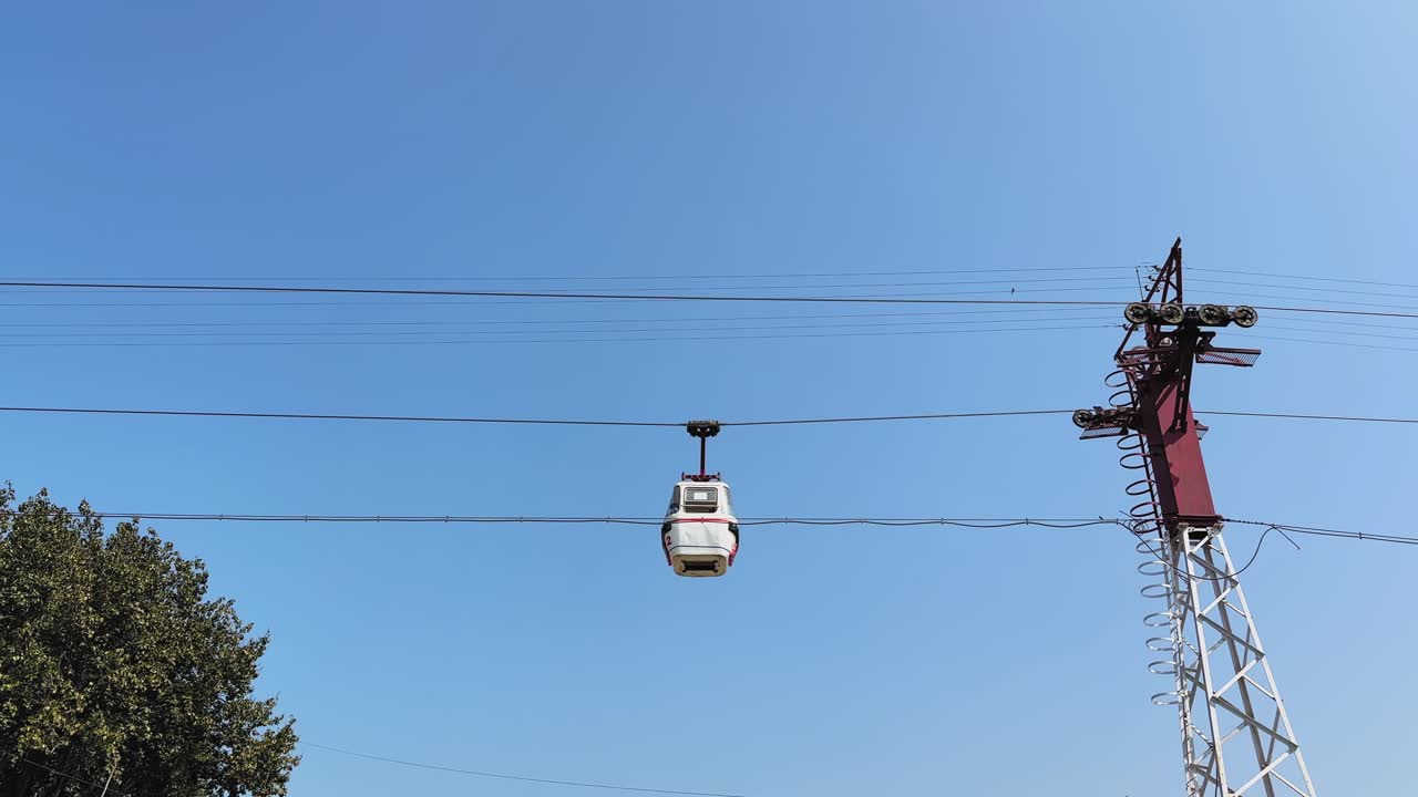 Gondola di una funivia che si muove lungo un cavo contro un cielo azzurro limpido, supportata da una torre metallica, mostrando un trasporto aereo utilizzato per il turismo e i viaggi.