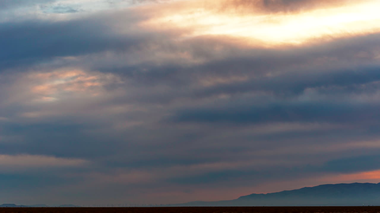 구름의 파도가 먼 안개 속에 있는 산과 함께 일몰 하늘을 가로질러 움직입니다 - 클라우드스케이프 시간 경과