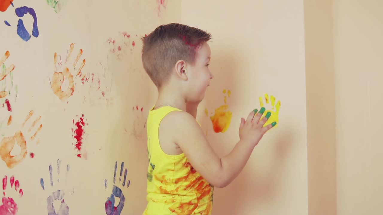 행복한 귀여운 작은 소년은 벽에 그의 다채로운 손자국을 남겨 즐기고 있습니다. 젊은 행복한 가족. 어머니와 자녀 개념